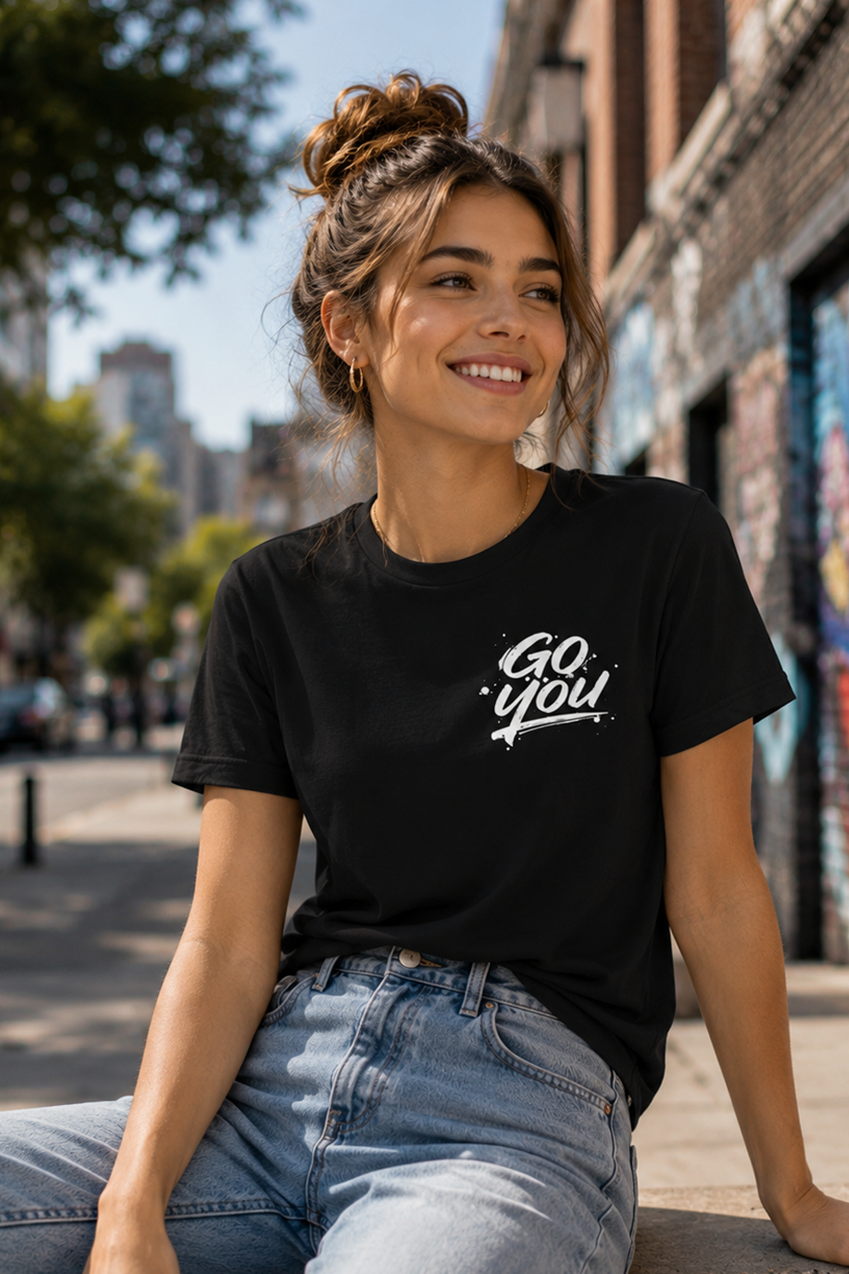 Woman wearing a black t-shirt with 'Go You' text, sitting on a city street.